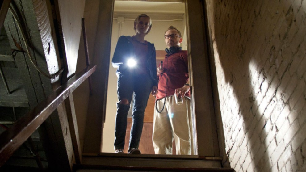 A woman and man holding a flashlight and looking down a flight of stairs.