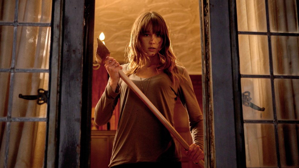 A woman holding an axe, standing in front of a window.